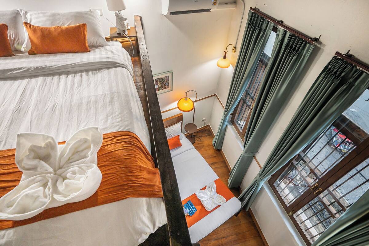 Een hotelkamer met een bed, nachtkastje, lamp en een raam met gordijnen.