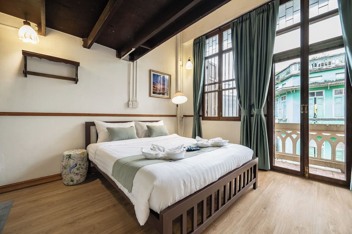 Hotelkamer met een houten bed, een nachtkastje, een lamp en uitzicht op een gebouw door een raam met gordijnen.