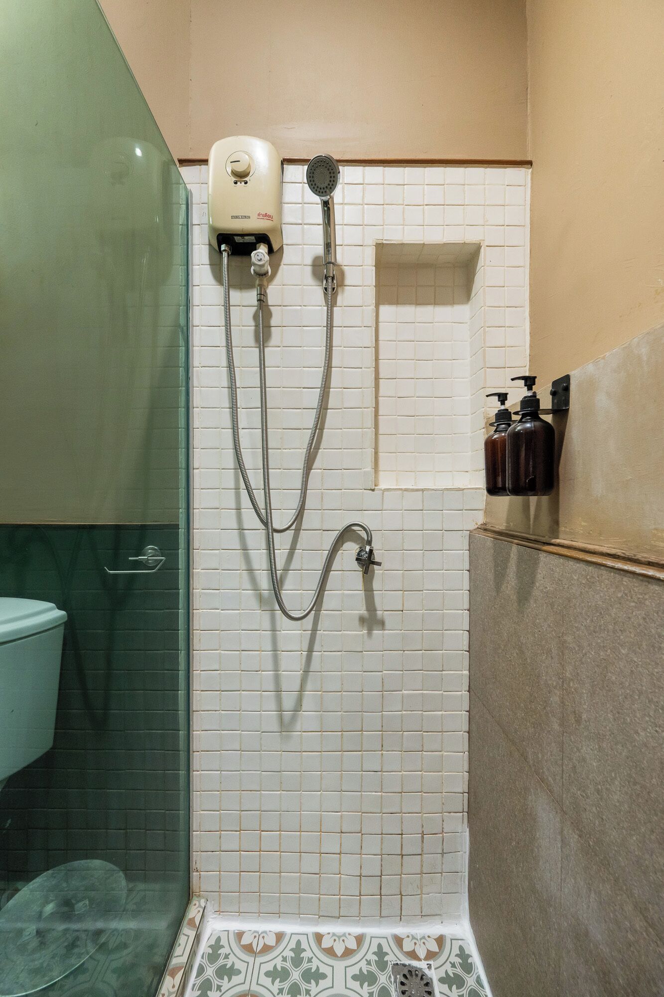 A shower with a glass enclosure, a white tiled wall, and a small shelf with toiletries.