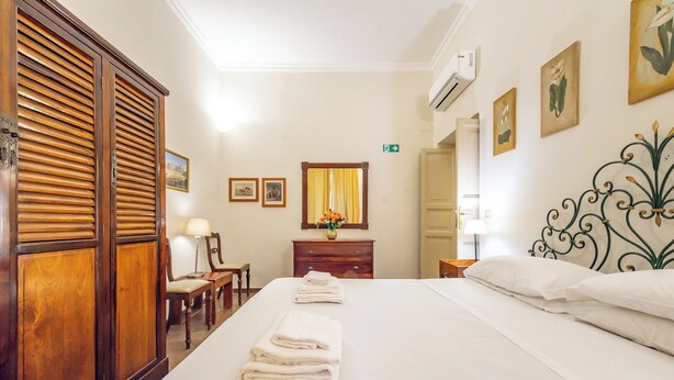 A hotel room with a large bed, wooden wardrobe, a desk with a chair, a mirror, and a small table with a lamp. - 3 House by Ghor (Rome)