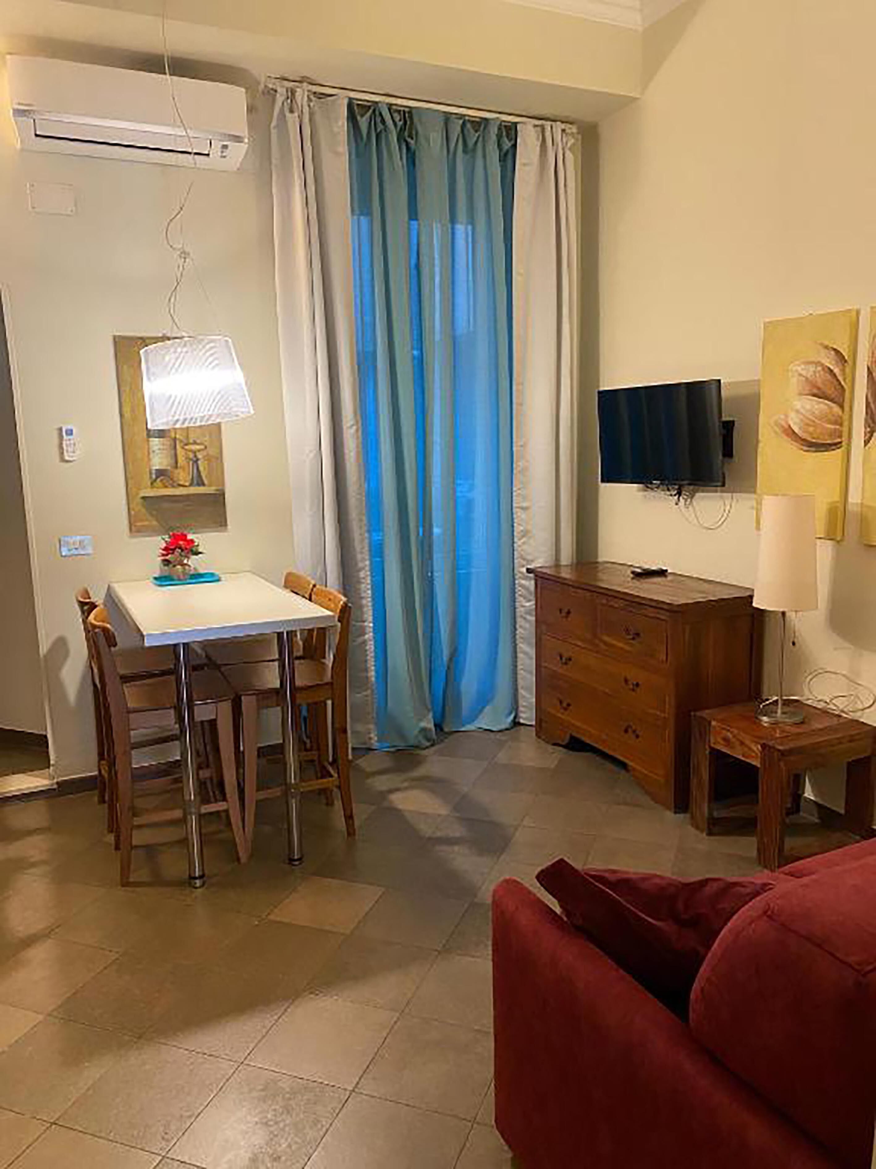 Ein kompakter Wohnbereich mit Essbereich, einem an der Wand befestigten Fernseher und einem roten Sofa.