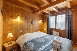 Ein Zimmer mit Holzwänden, einem Bett, zwei Wandleuchten, einer Heizung und einem Fenster mit Vorhängen.