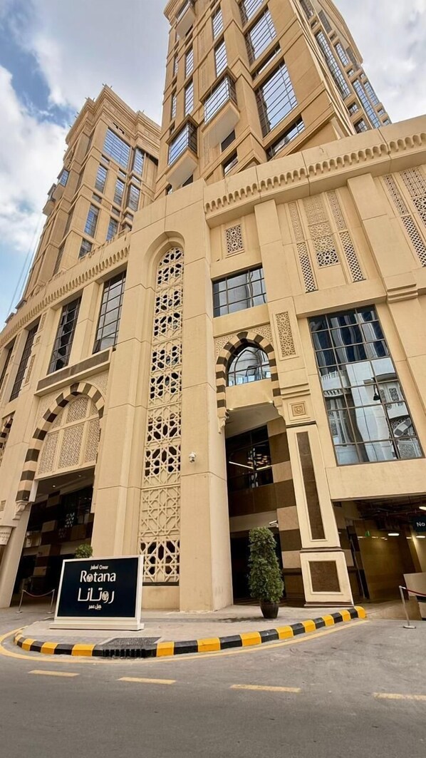 A large, beige building with intricate architectural details, a sign reading 'Rotana Li'loo,' and a parking area with yellow and black curbs.