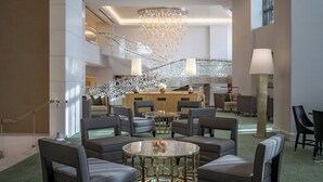Um hall de hotel moderno com uma recepção central, diversas áreas de estar e uma escadaria decorativa.
