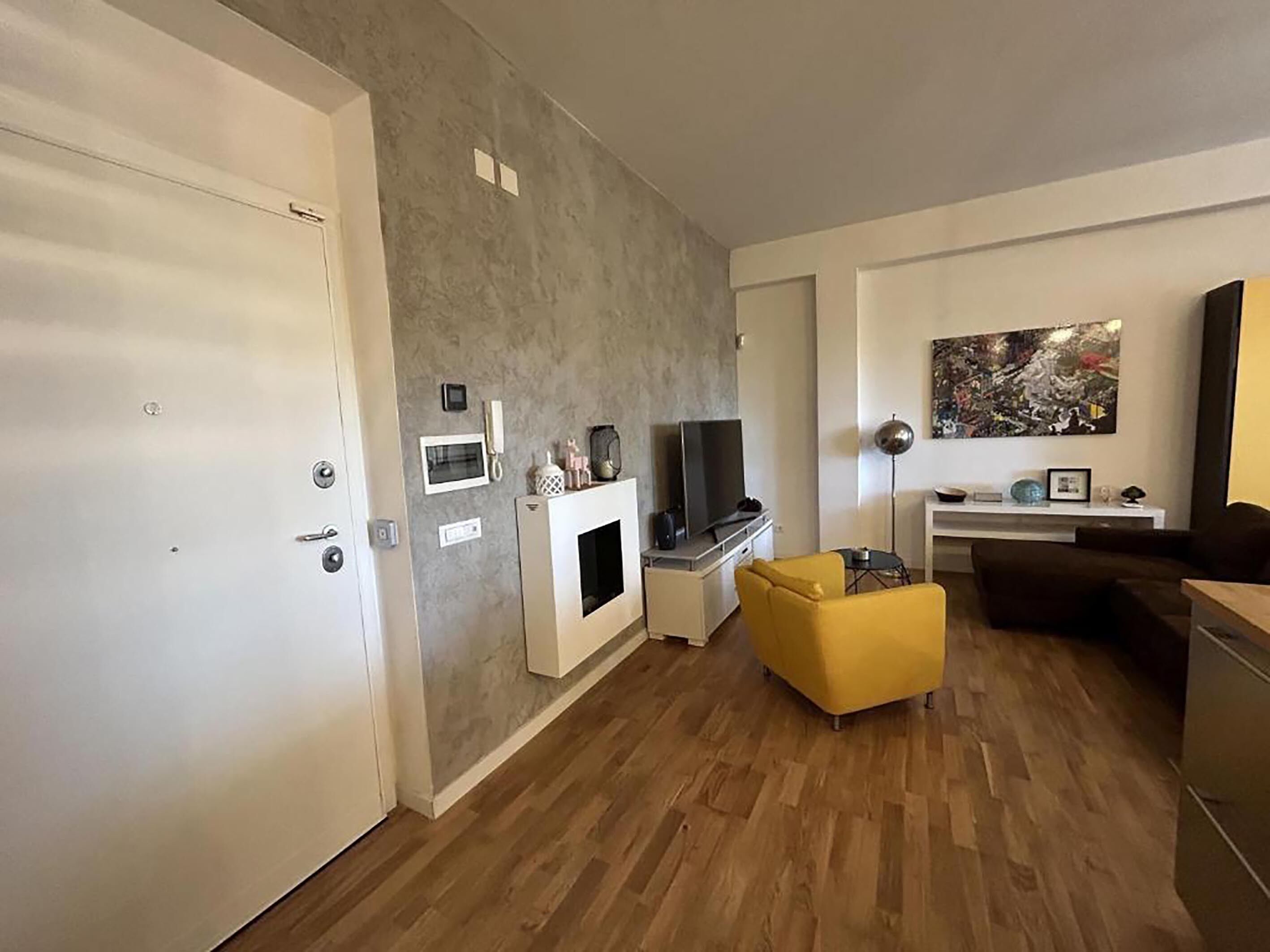 Ein modernes Wohnzimmer mit Holzboden, einer Couch, einem gelben Sessel, einem Fernseher und einem Bild an der Wand.