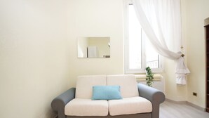 A neutral-colored sofa with a blue cushion in a bright room with a large window and a mirror on the wall. - Rafael House by Ghor (Rome)