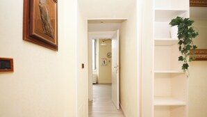 A narrow hallway with a wooden door at the end, a white shelf unit on the right, and a framed picture on the left. - Rafael House by Ghor (Rome)