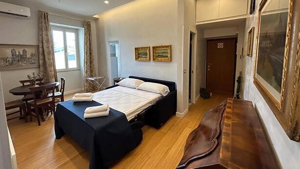 A hotel room with a bed, a dining table, and chairs. There is a painting on the wall and a door leading to another room. - Manzoni Blue House by Ghor (Rome)