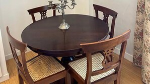 A round wooden dining table with a candelabra centerpiece, surrounded by four wooden chairs with woven seats. A framed cityscape painting hangs on the wall above the table. - Manzoni Blue House by Ghor (Rome)