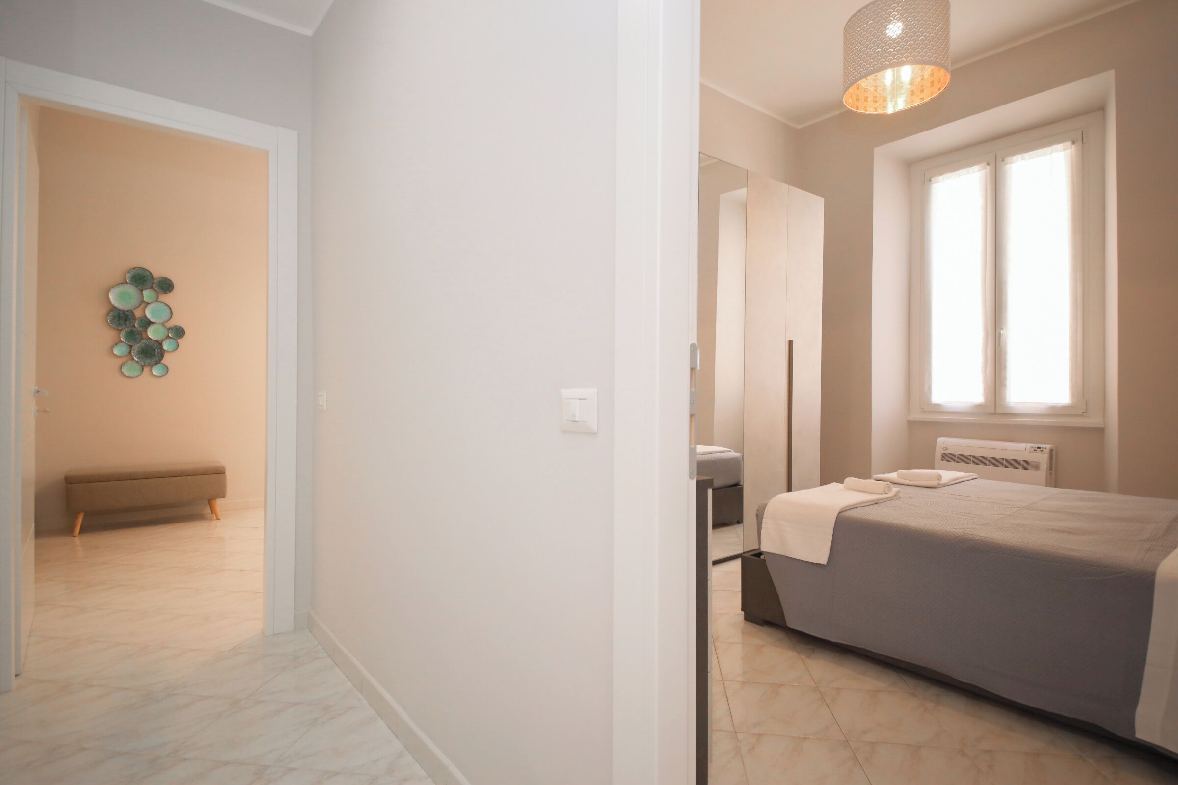 Un dormitorio con cama, mesita de noche, lámpara, ventana y un adorno en la pared.