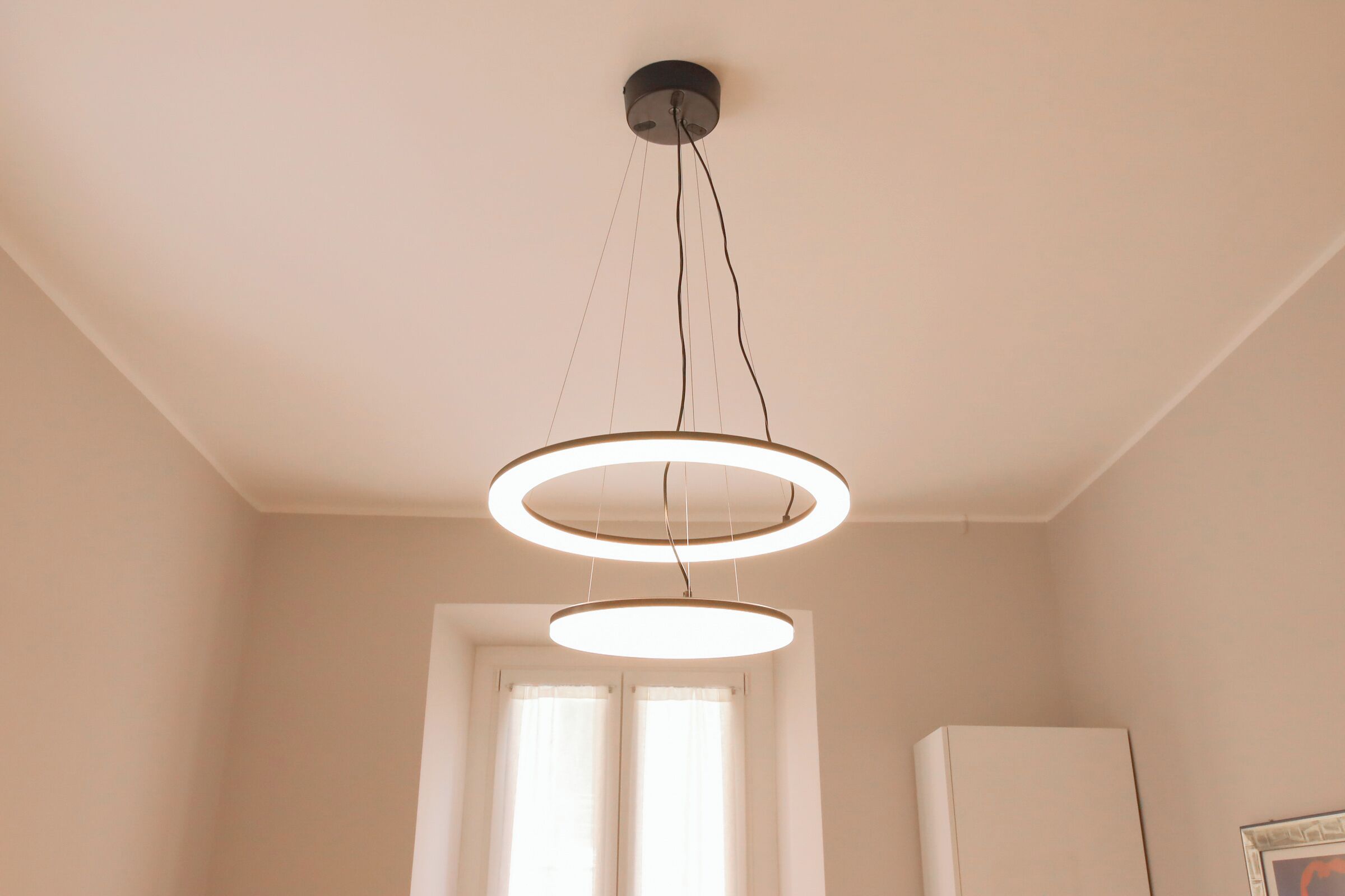 Un luminaire moderne pour plafond, composé de deux anneaux concentriques et d’un seul câble de suspension.
