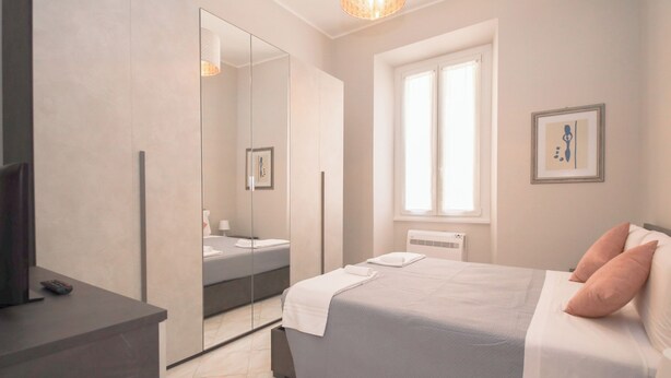 A modern bedroom with a large bed, a bedside table, a mirror, and a window. - Rome Flat 42 by Ghor (Rome)