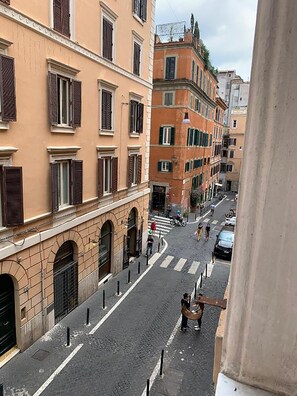 Una veduta di strada con edifici dalle finestre ad arco e persiane, un attraversamento pedonale e cielo sereno.