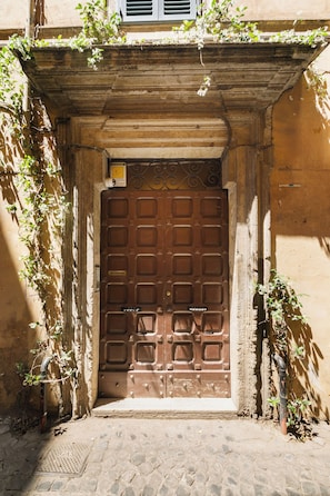 A brown wooden door with a decorative metal frame, set in a stone wall with a small window above. - Elegant Apartment Minelli Navona by Ghor (Rome)