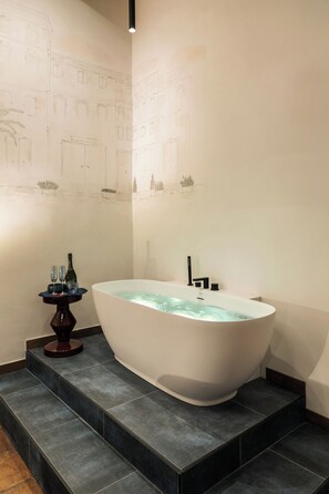 A modern bathroom with a freestanding bathtub, dark tiled flooring, and a small side table with two glasses and a bottle. - Elegant Apartment Minelli Navona by Ghor (Rome)