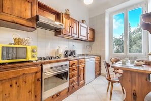 A kitchen with wooden cabinets, a yellow microwave, a stove, and a window with a view of trees. - Emanuele House by Ghor (Rome)