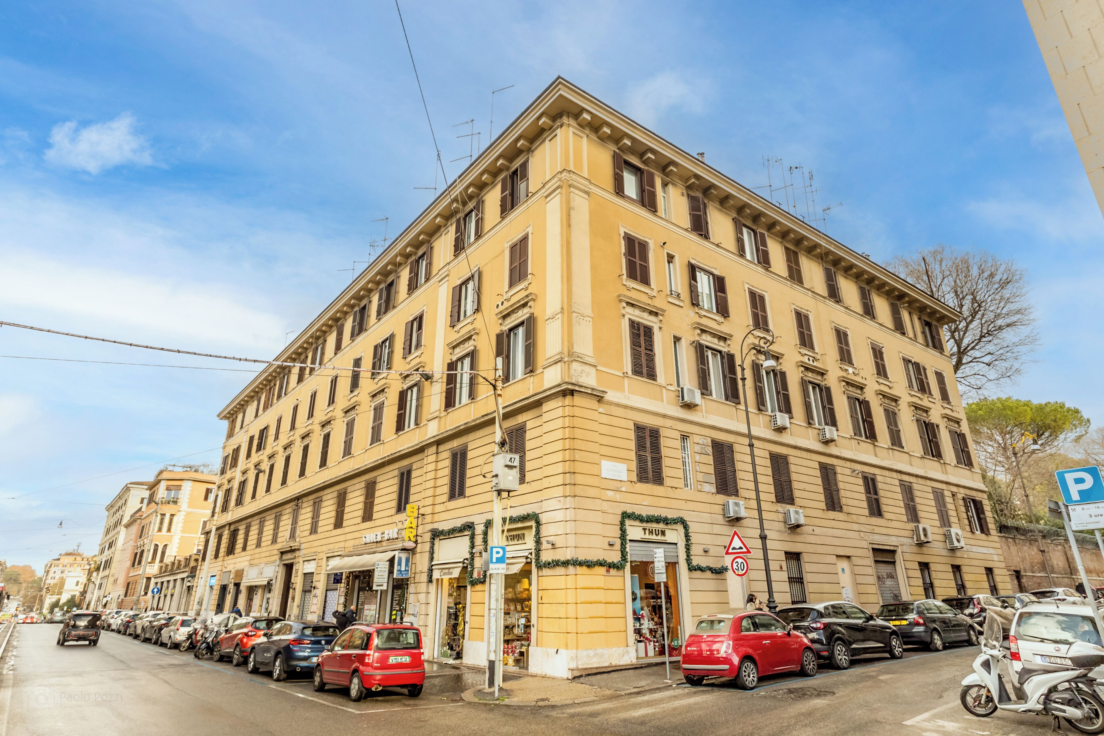 A multi-story building with a classic architectural style, featuring a ground floor with commercial establishments and a parking area.
