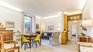 Un vaste espace de vie comprenant une table à manger, des chaises jaunes, un canapé, un fauteuil en osier et une bibliothèque.