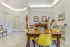 A dining area with a wooden table, yellow chairs, framed pictures on the wall, and a white door. - Emanuele House by Ghor (Rome)