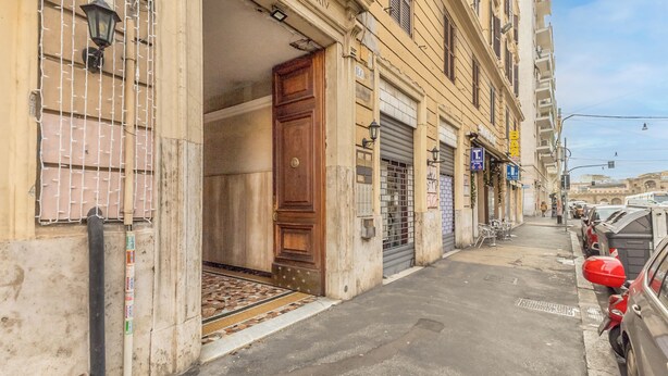 Une rue étroite bord ée de voitures garées, une entrée d’immeuble avec une porte en bois et un portail en métal.
