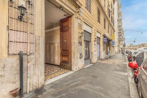 A narrow street with parked cars, a building entrance with a wooden door, and a metal gate. - Emanuele House by Ghor (Rome)