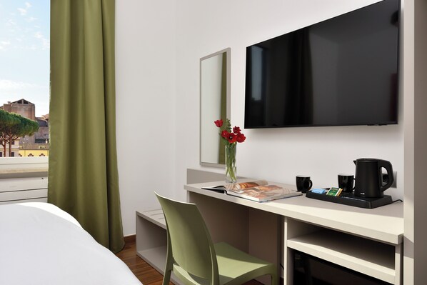 A hotel room with a bed, a desk with a computer, a TV, a coffee maker, and a vase with flowers. - Colosseo Panorama - Camera 401 by Ghor (Rome)