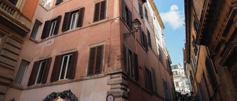 A narrow street with historic buildings, including a pink building with shutters and a visible no parking sign.