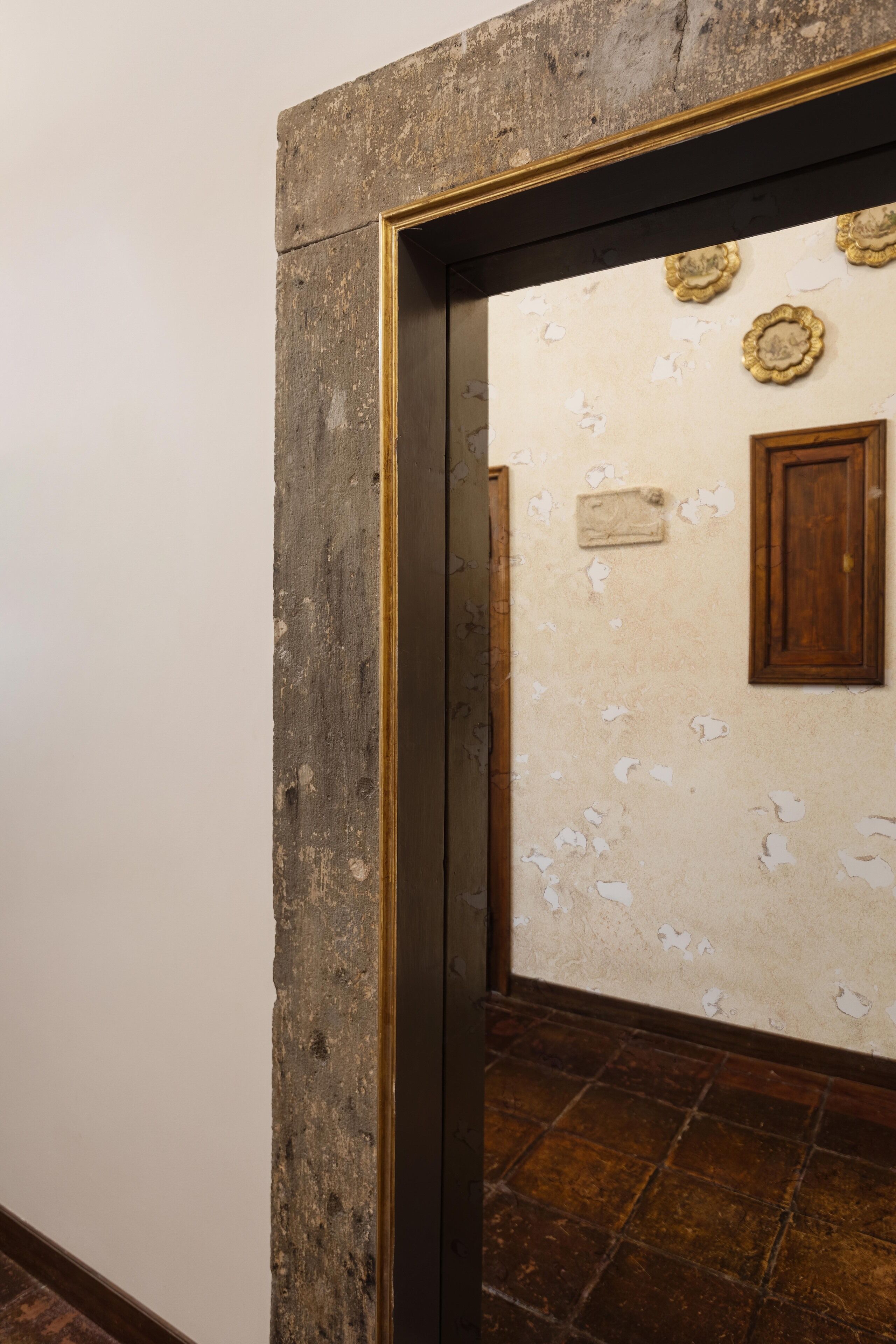 A doorway with peeling paint and a wooden door, leading to a room with a tiled floor and a wall-mounted plaque.