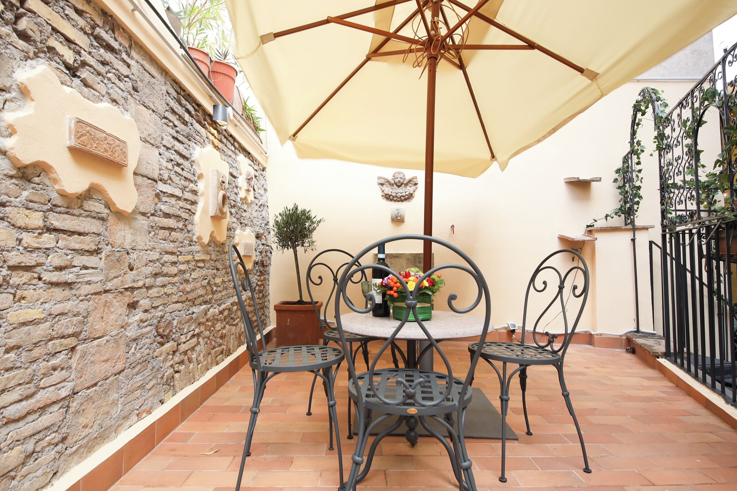 A patio with a round table, four chairs, a large umbrella, and potted plants.