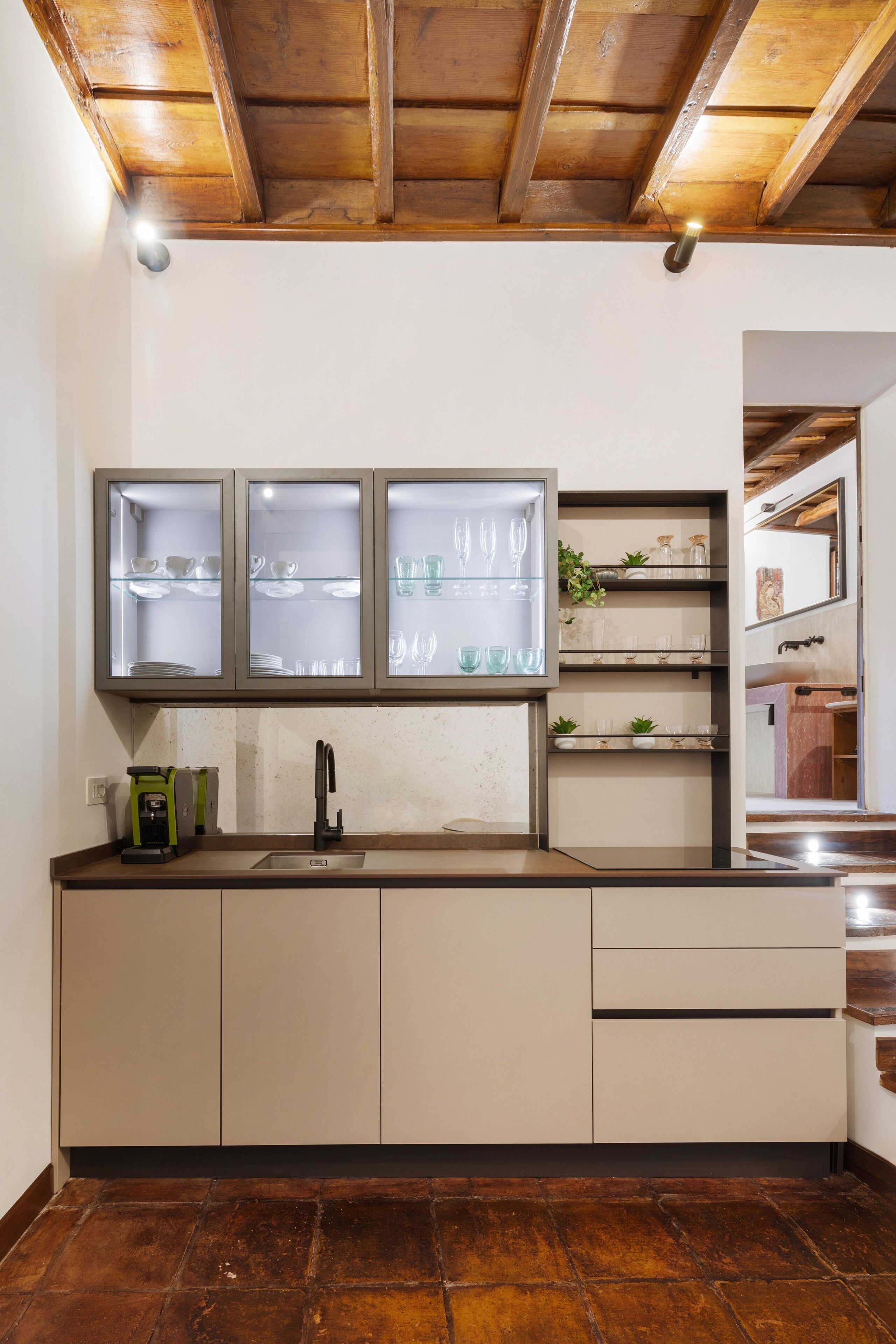 Eine Küche mit Holzbalkendecke, einem eingebauten Schrank mit Glastüren, einer Spüle und einer Kaffeemaschine.
