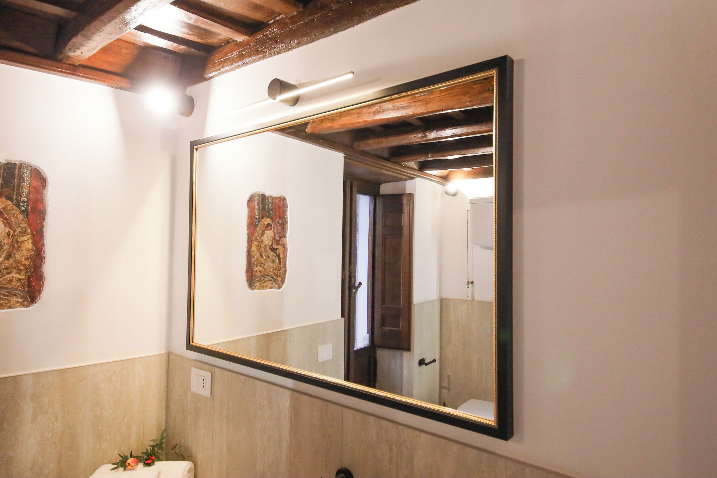Une salle de bain dotée d’un grand miroir, de poutres en bois et d’une serviette agrémentée d’un motif floral.