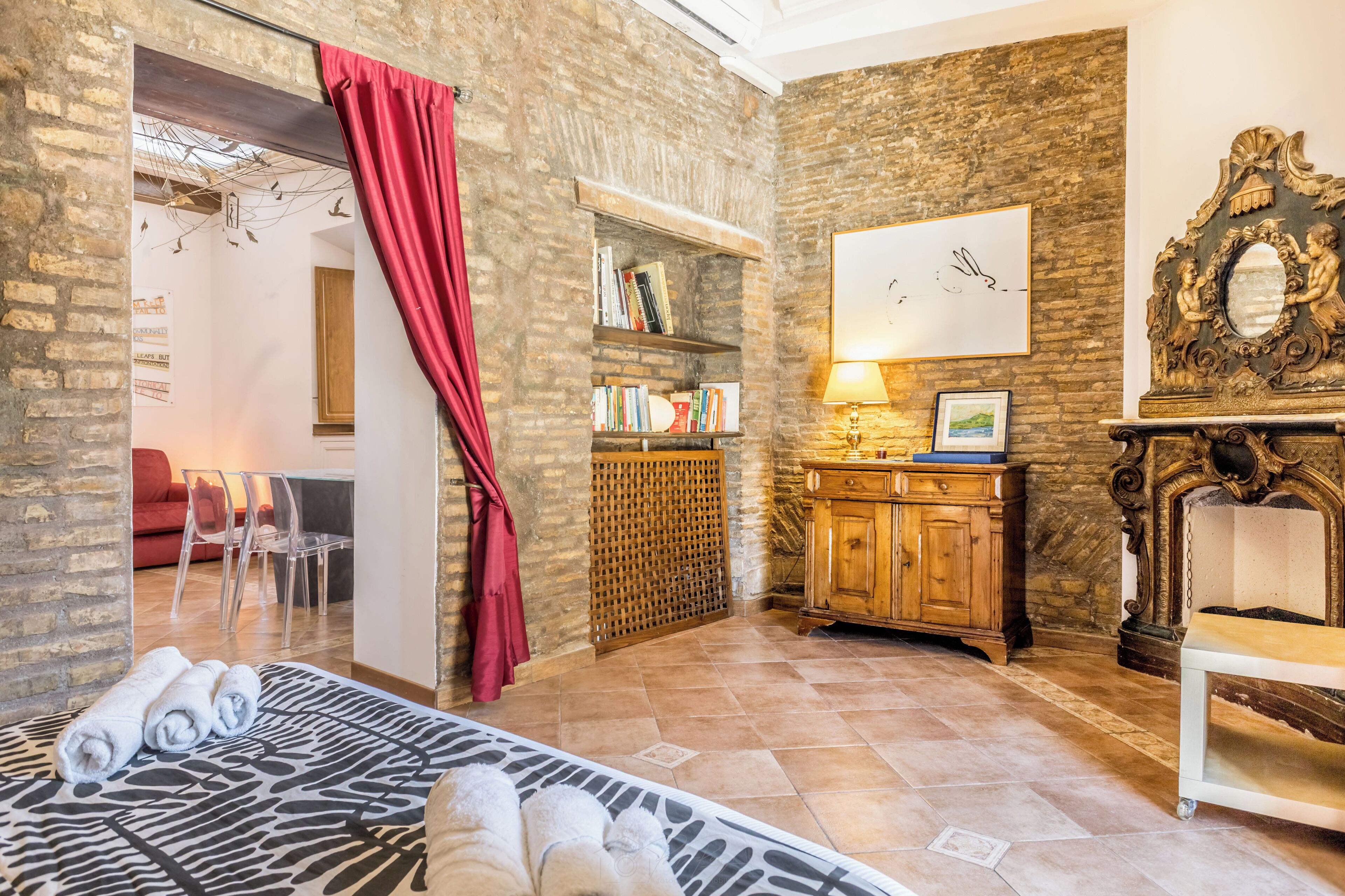 A room with a bed, a wooden cabinet, a fireplace, and a red curtain.