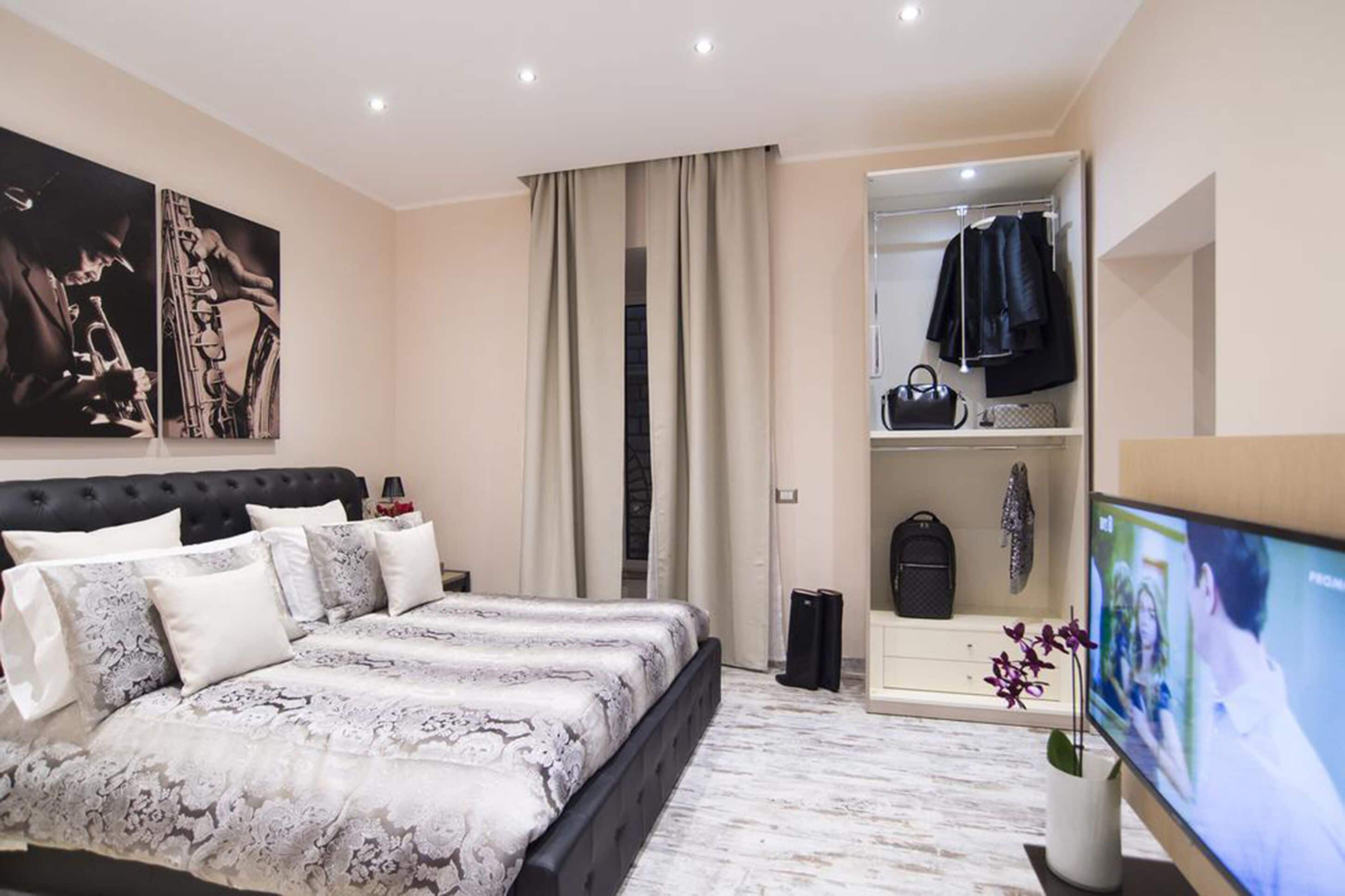 A modern bedroom with a large bed, a built-in wardrobe, a television, and artwork on the wall.