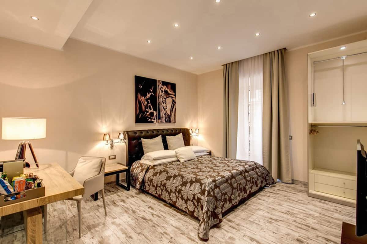 Una habitación de hotel con cama, escritorio, laptop, silla y armario.
