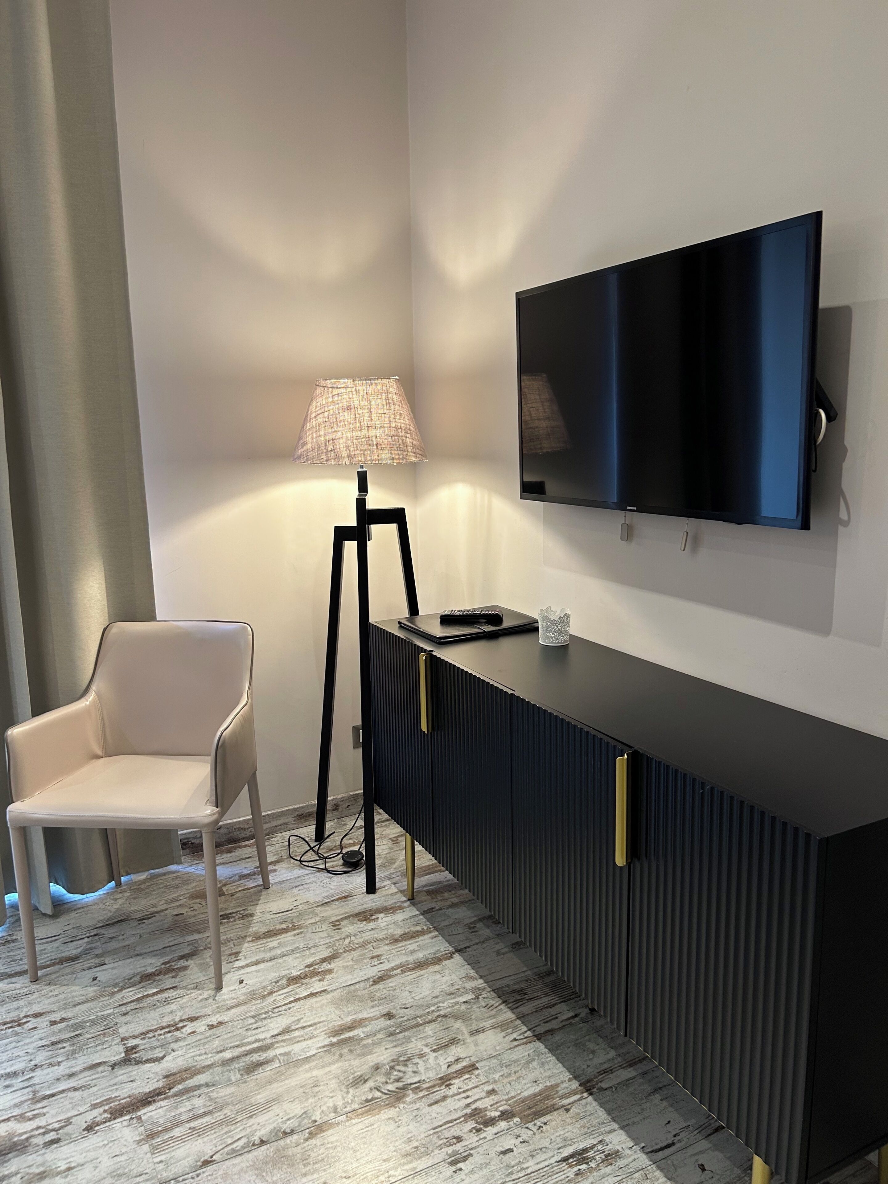 Una stanza con un moderno tavolo consolle nero, una TV a schermo piatto montata, una sedia bianca e una lampada da terra.