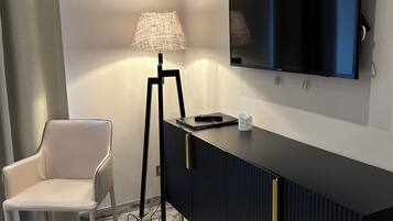 Una stanza con un moderno tavolo consolle nero, una TV a schermo piatto montata, una sedia bianca e una lampada da terra.