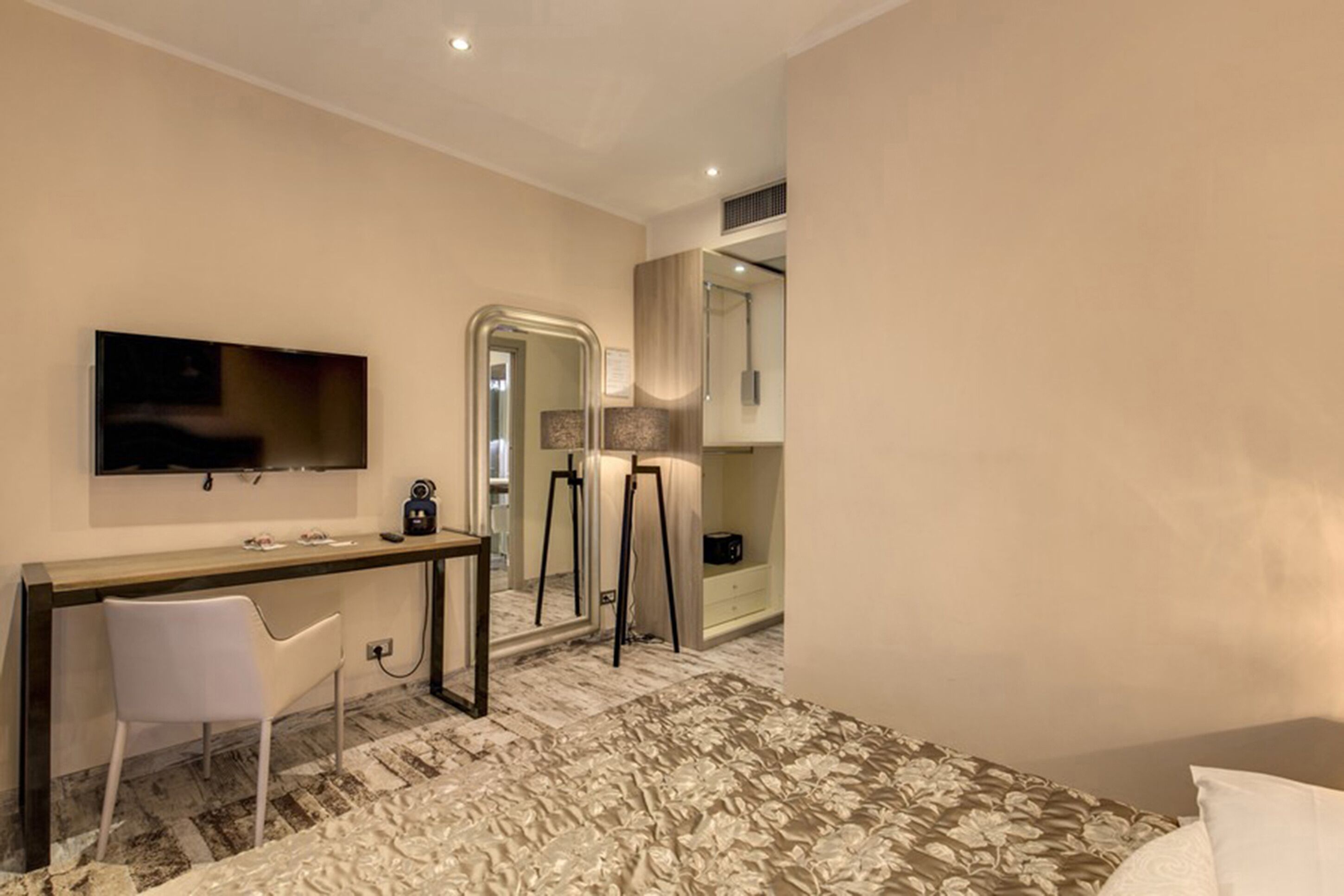 Quarto de hotel moderno com televisão de tela plana, escrivaninha com cadeira, espelho grande e carpete estampado.