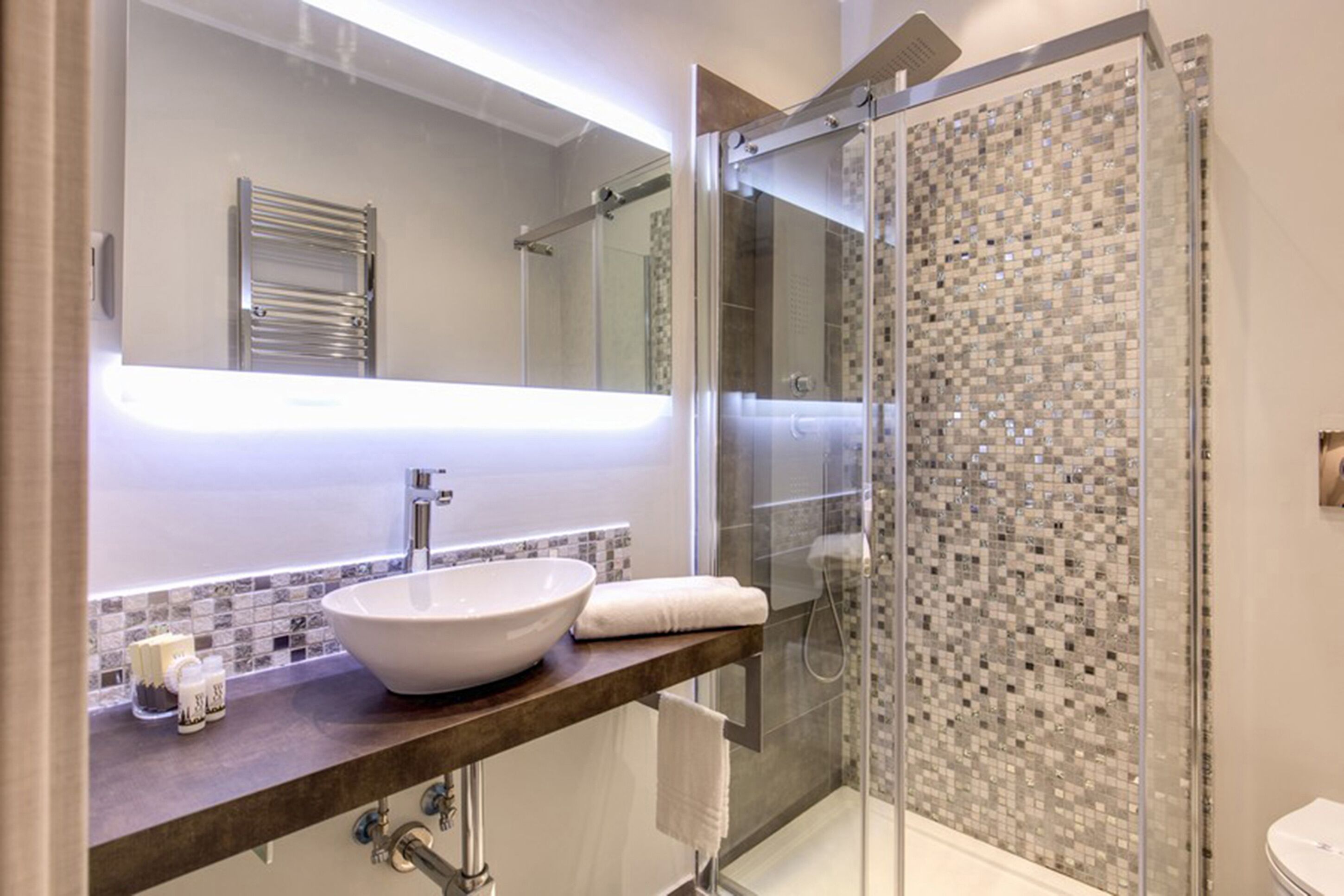 Un baño moderno con un espejo grande, un lavabo sobre encimera, una ducha con cerramiento de vidrio y un salpicadero de azulejos.