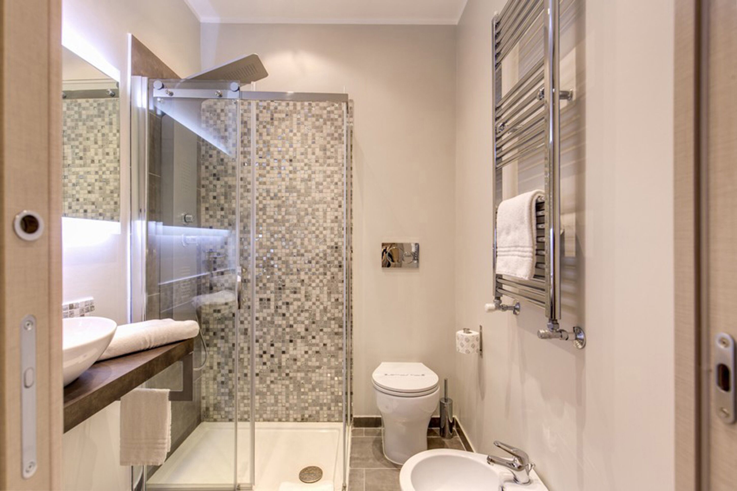 A bathroom with a glass-enclosed shower, a toilet, a bidet, and a sink with a towel rack.