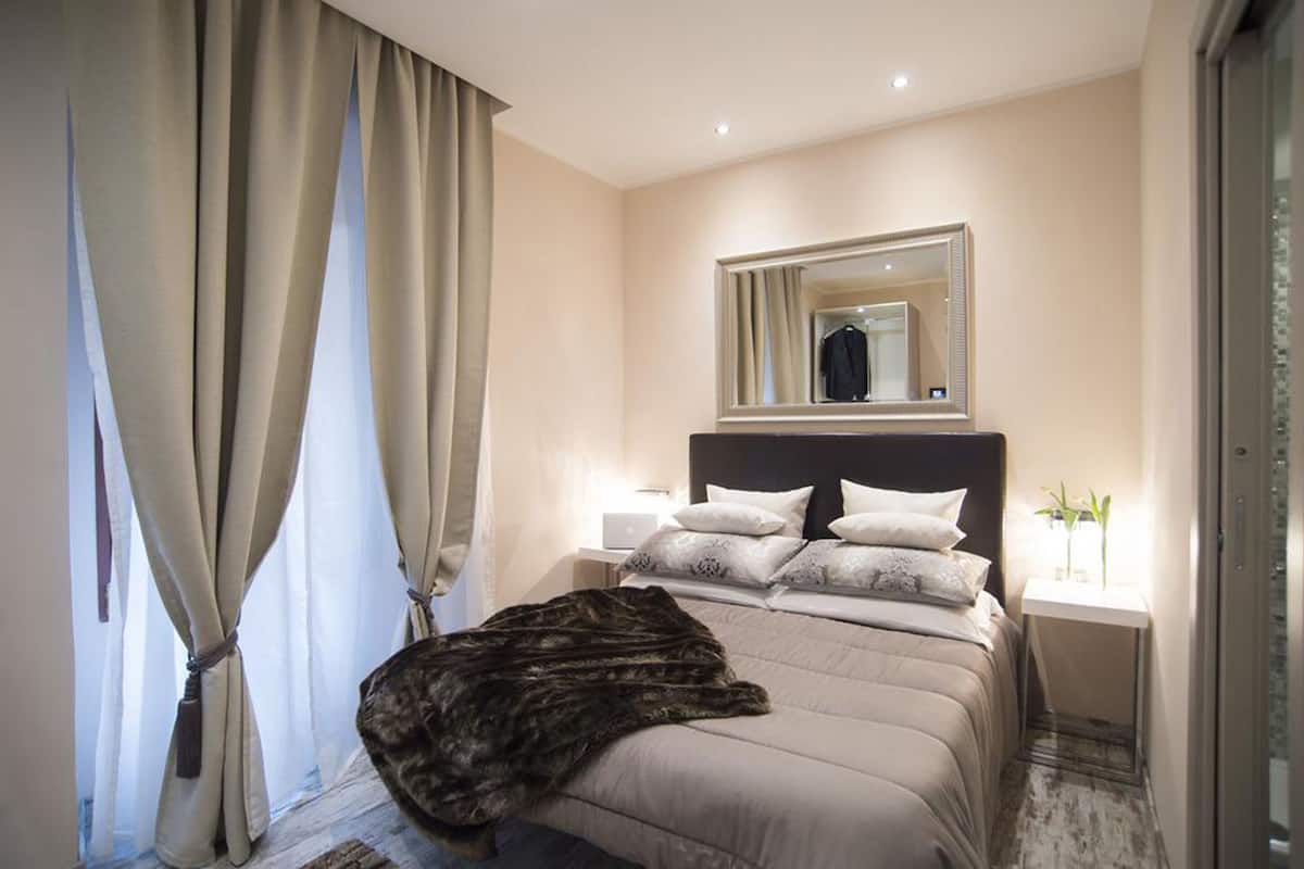 Un dormitorio moderno con una cama grande, una mesita de noche, un espejo y una ventana con cortinas.