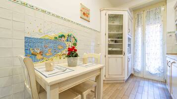 Une cuisine avec un mur recouvert de carreaux, une table à manger avec des chaises, un meuble et une fenêtre avec des rideaux.