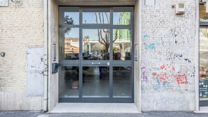 Una entrada de edificio con puerta de vidrio, un letrero visible y grafitis en la pared.