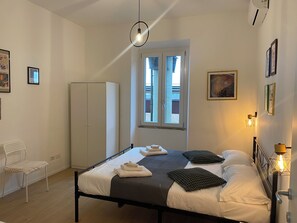 A bedroom with a bed, a wardrobe, a chair, a window, and a wall-mounted light fixture. - Casa Arcangela by Ghor (Rome)