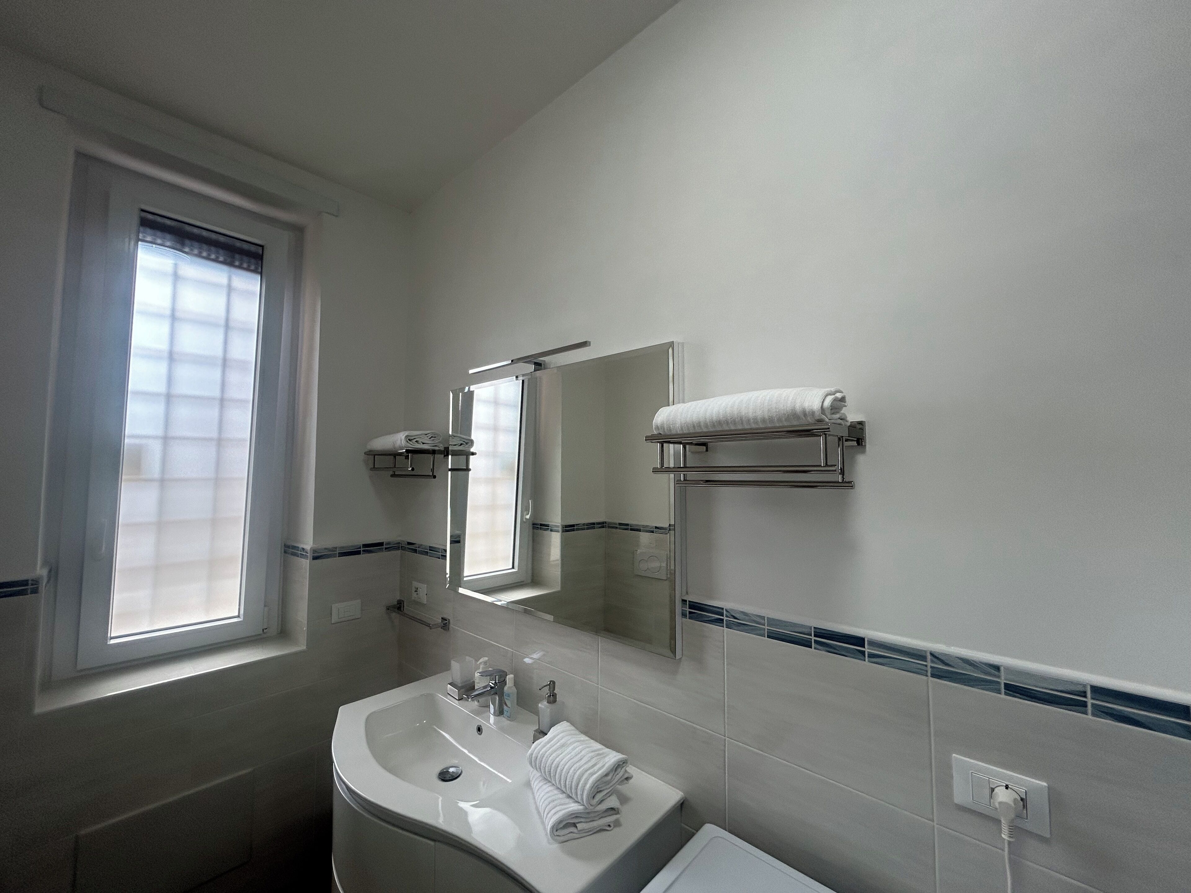 A bathroom with a sink, mirror, towel rack, and window.