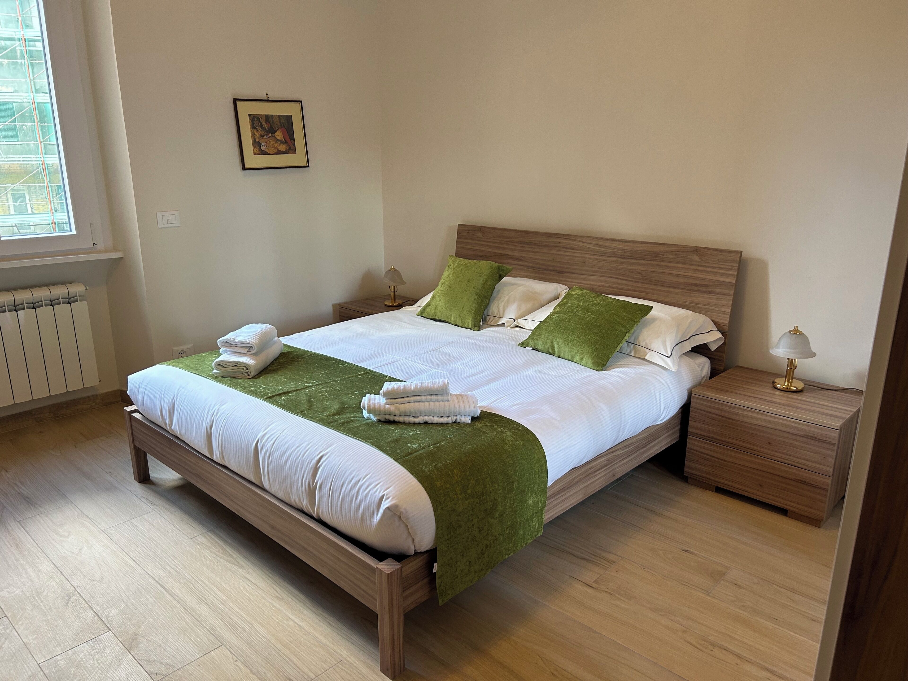 Un lit bien fait, avec un couvre-lit vert, des oreillers blancs et des serviettes pliées, posé sur un cadre de lit en bois.