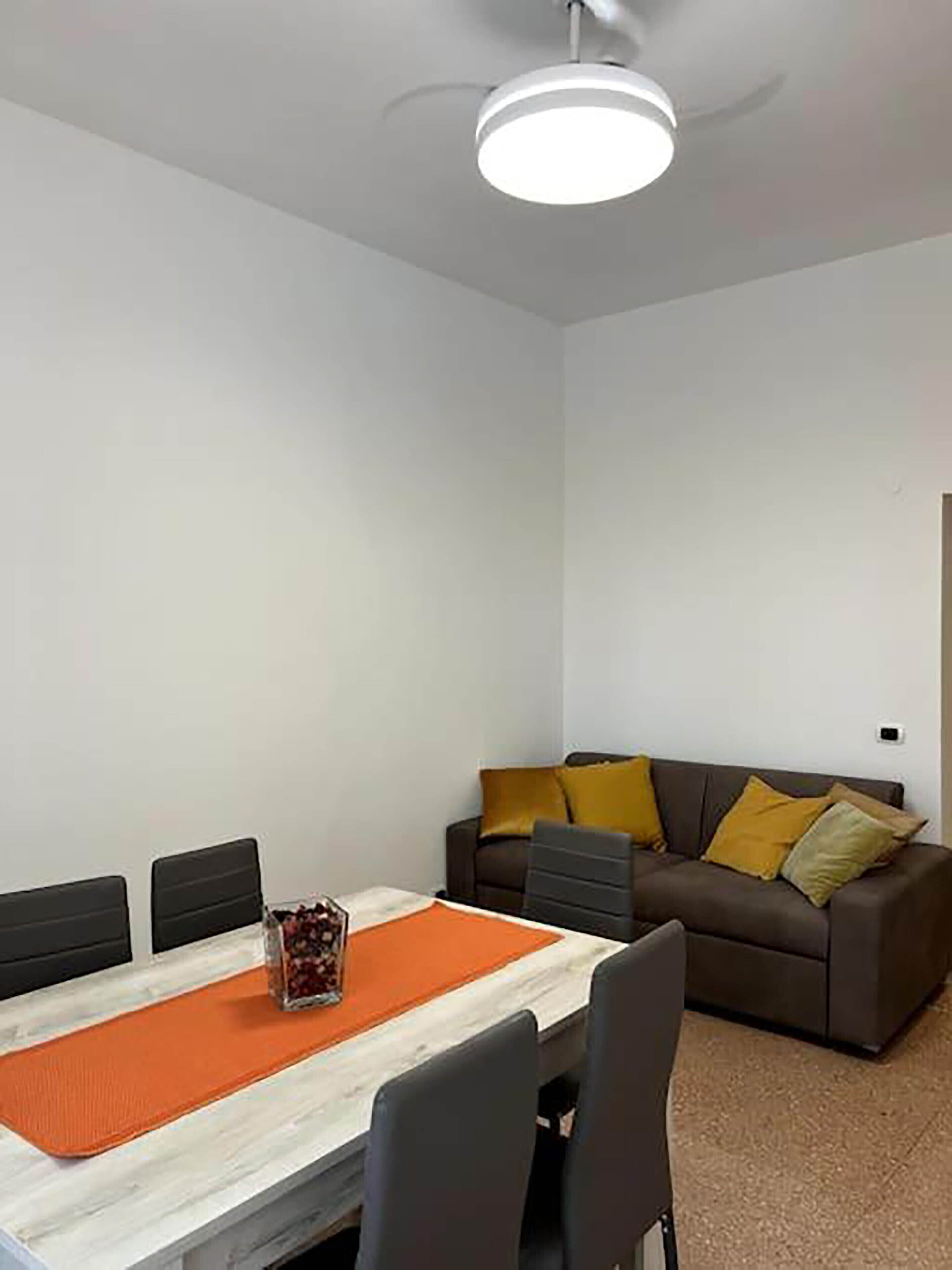 A modern living room with a dining table, a sofa, and a ceiling light.