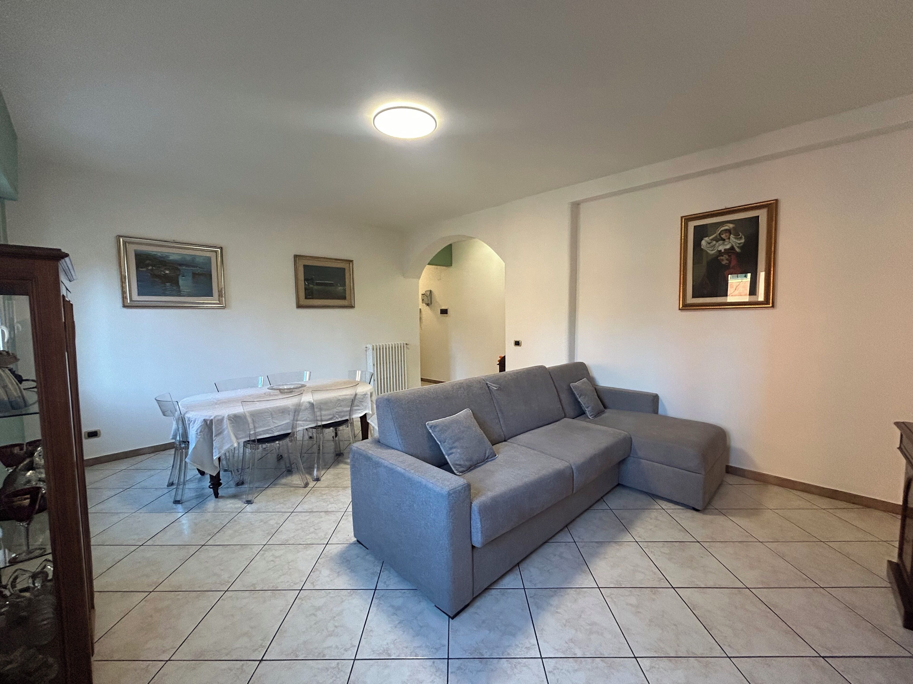 Un salon avec un canapé gris, une table à manger avec des chaises et deux tableaux encadrés accrochés aux murs.