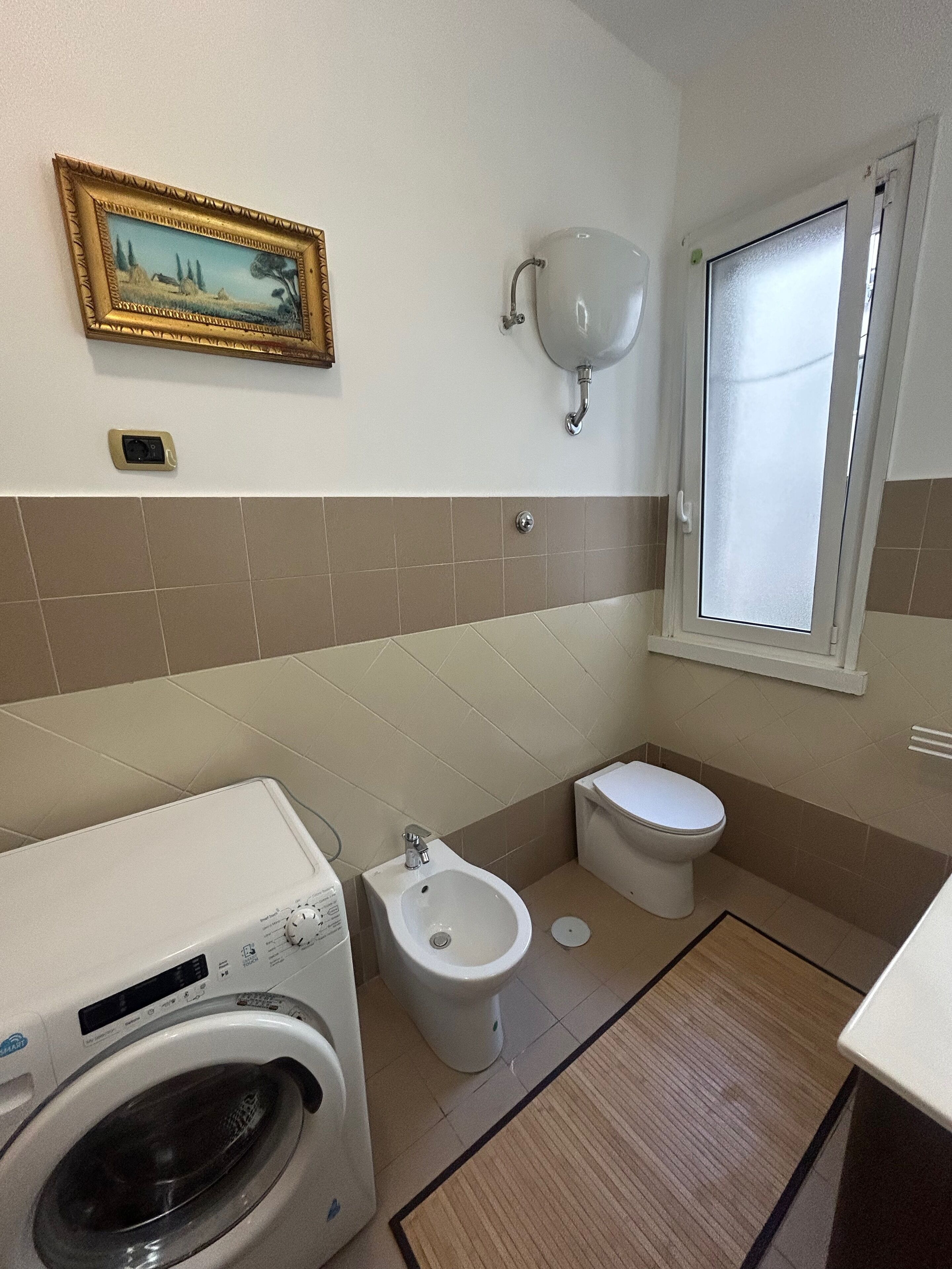 A compact bathroom with a washing machine, bidet, toilet, and a framed picture on the wall.