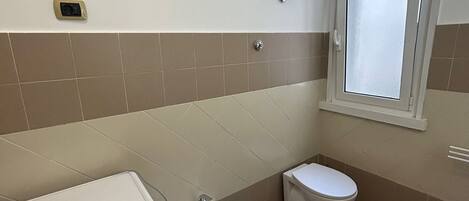 A compact bathroom with a washing machine, bidet, toilet, and a framed picture on the wall.