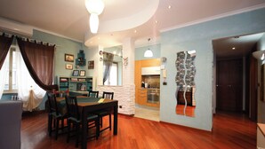 A dining area with a wooden table and chairs, a kitchen in the background, and a living room with a sofa and a TV. - Archidee by Ghor (Rome)